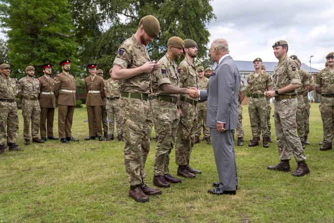 The King presents promotions to three Grenadier Guardsmen as their comrades look on, outside in their barracks in Aldershot