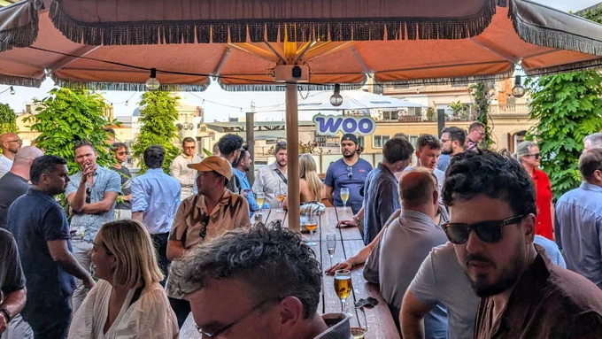 A crowd gathers on a rooftop patio, and the Woo logo can be seen in the background.