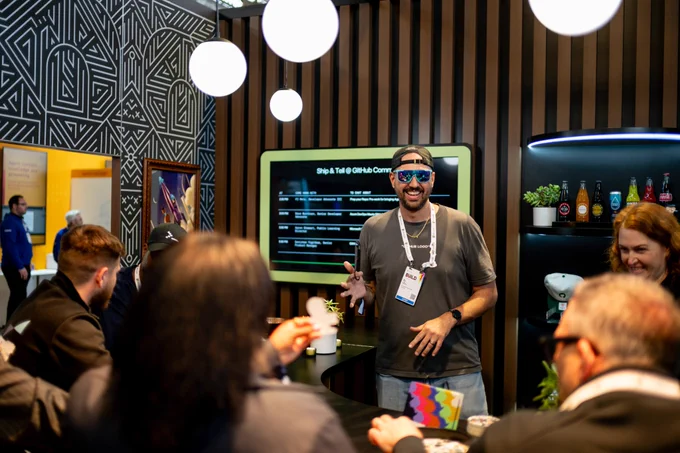 Pj behind a bar with blue shiny sunglasses on, spinning a bar key and smiling. 