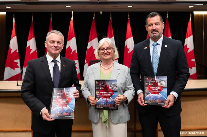 A group of people standing in front of Canadian flags. 