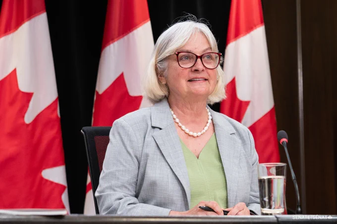 A woman sitting in front of a microphone, with Canadian flags in the background.