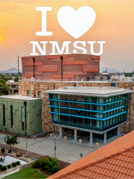 A scenic view of New Mexico State University campus buildings at sunset, with an overlay text at the top saying "I ❤️ NMSU."
