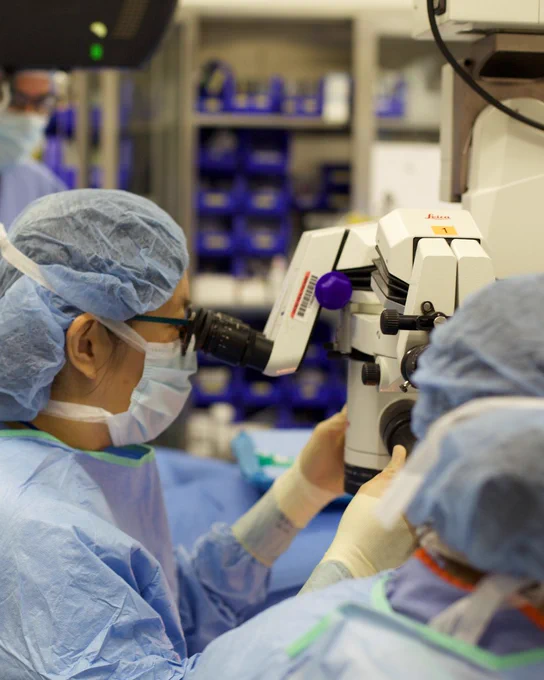 Surgeon wearing personal protective equipment looking in microscope in operating room. 