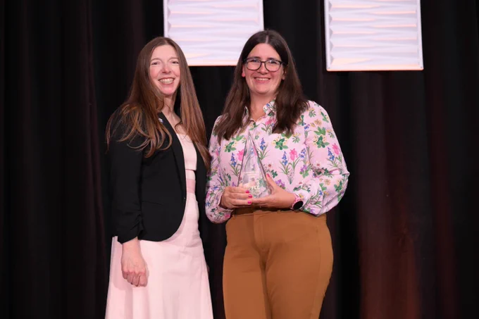Two people smiling, one holding an award. 