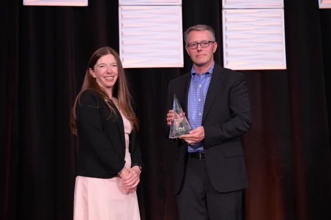 Two people smiling, one holding an award. 