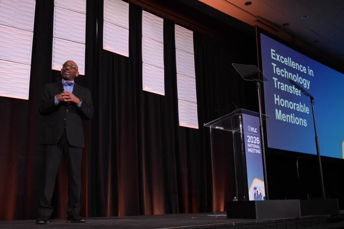 Man stands on a stage, a screen behind him with text "Excellence in Technology Transfer Honorable Mentions" 