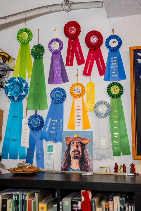 A wall decorated with colorful award ribbons showcasing achievements in art events. Various colors and texts create a vibrant scene.