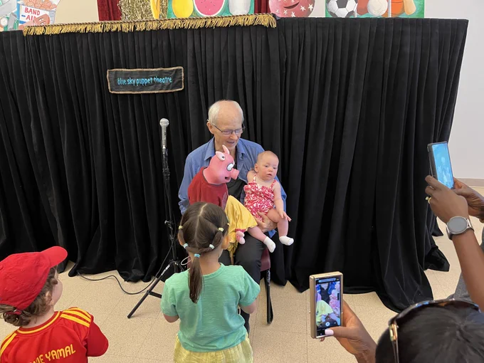 Man holds baby as he performs puppet show.
