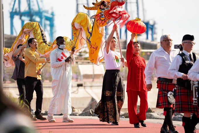 Group performing a traditional dragon dance outdoors with participants holding the dragon and a red lantern during a cultural event.