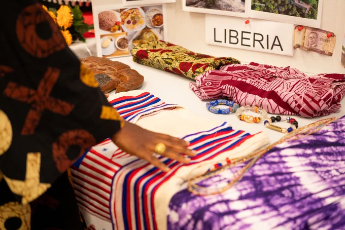 Hand touching colorful striped fabric on a table displaying Liberian textiles and traditional crafts.