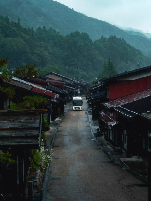 A rainy day in Shirakawa-go, Japan, with traditional thatched-roof houses, lush green rice fields, and quiet village streets glistening after the rain. A person carrying a red umbrella walks through the countryside, surrounded by misty hills. The whole scene feels like something straight out of a Studio Ghibli film.

Photography by Andrew Zhao (@andyescapes)