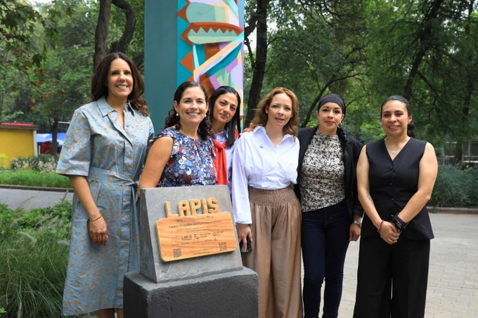 Seis personas sonríen junto a una placa que dice "LAPIS" al aire libre, rodeadas de un entorno arbolado y un mural colorido.