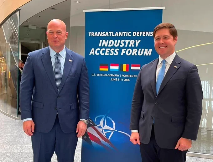 Photo of DAS McKinney and Ambassador Whitaker standing next to a sign for the Transatlantic Defense Industry Access Forum. 