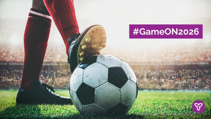 A soccer player rests one foot on a soccer ball on a stadium field beside text reading “#GameON2026.”