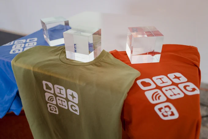 Colorful Bitrig t-shirts with logos and three awards are displayed on tables, showcasing memorabilia from the Bitrig Hacks event.