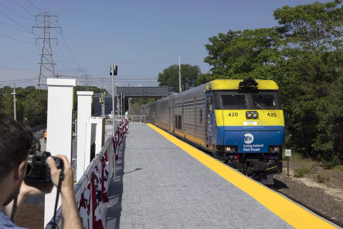 An LIRR diesel train approaching the Shinnecock Hills temporary station. A person is taking a photograph of the train. 