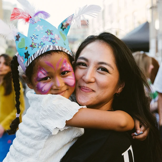A mother hugs her daughter who is wearing a crown and butterfly face paint.