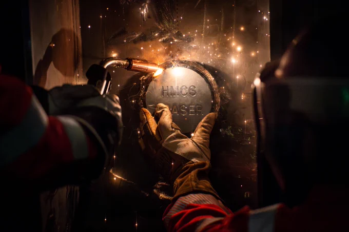Welder wearing protective gloves and helmet welding a metal plate with sparks flying around. 