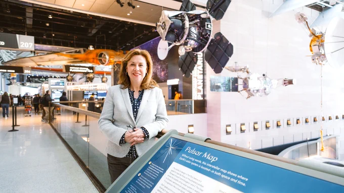 Margaret Weitekamp with red hair and a suit jacket standing next to a spacecraft on the floor of the Air and Space Museum.