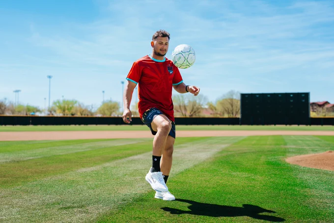 Gabriel Moreno plays with a soccer ball on a field at Salt River Fields. He is wearing a red and teal Gabriel Moreno Soccer Jersey. 