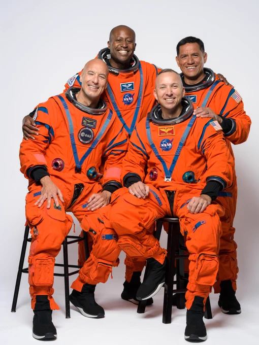 The four crew members of Artemis III -- from left to right, Luca Parmitano, Andre Douglas, Randy Bresnik, and Frank Rubio -- grin for the camera as they pose for a photo. They are wearing their orange flight suits against a white background; Luca and Randy are seated on stools, with Andre and Frank standing behind them. Credit: NASA/Helen Arase Vargas