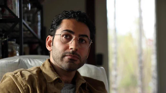 Mohsen Mahdawi pauses as he speaks to a Globe reporter in Fairlee, Vt., May 7, 2025. He is a young man with light brown skin, dark curly hair, and a short beard, wearing glasses and a corduroy jacket.