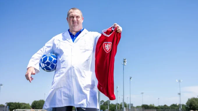 Photo of UTA chemistry professor Kevin Schug in a lab coat holding a soccer ball and a soccer jersey and standing on a soccer field.