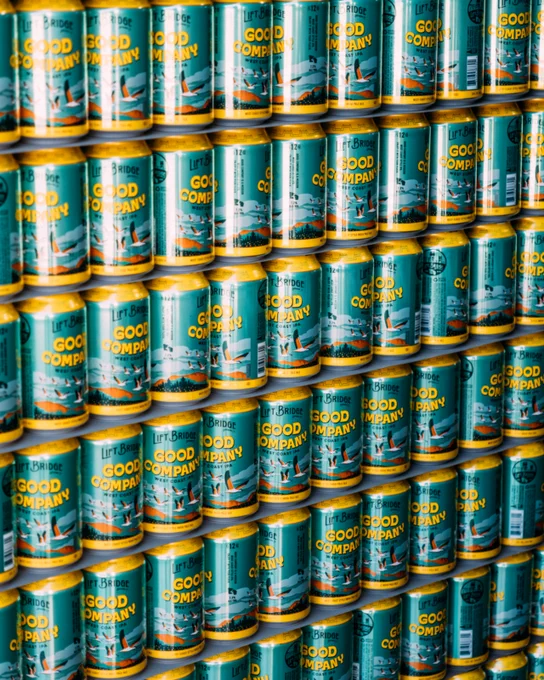 An organized display of vibrant beverage cans with teal and yellow colors, each labeled 'Good Company'. The arrangement creates an appealing pattern.