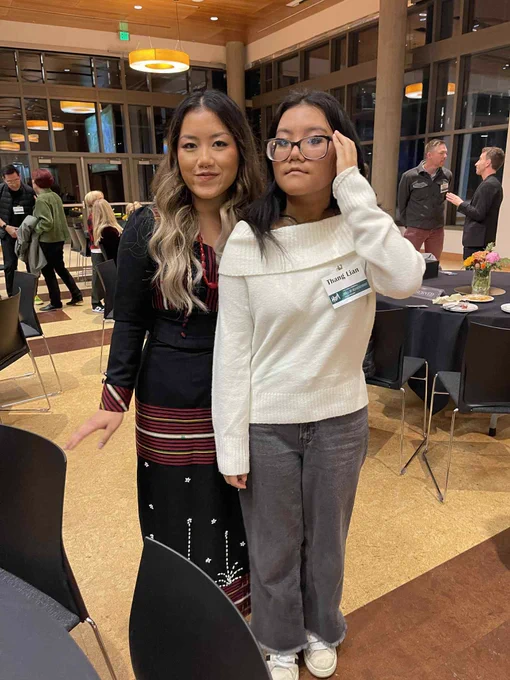 Two people standing in the Ford Alumni Ballroom wearing formal attire. People are socializing in the background