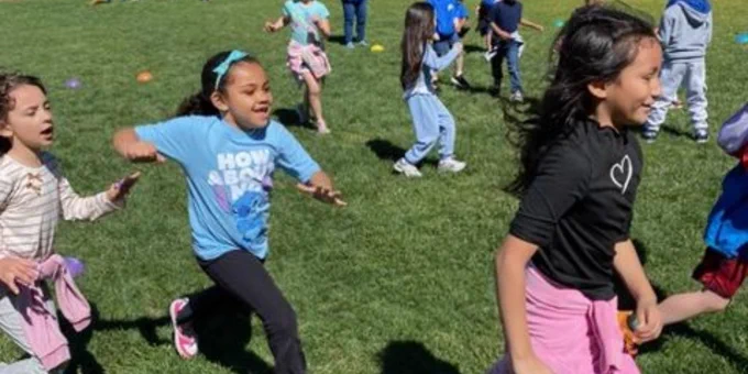 Children running and playing together on a sunny grassy field during outdoor activities.
