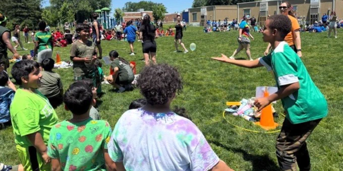 Children playing and socializing on a sunny school field during an outdoor event with various activities and groups scattered around.