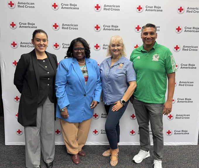 Four participants pose for a group photo in front of an American Red Cross and Cruz Roja Americana backdrop during an emergency preparedness training event. The group is smiling and standing side-by-side, representing community partners and local government staff committed to strengthening disaster response and preparedness efforts. The photo highlights the collaboration between the Department of Neighborhoods and the American Red Cross as they work together to enhance shelter operations training and support the Houston Emergency Response Team (HERT) program, helping ensure Houstonians are prepared and protected during emergencies and severe weather events.