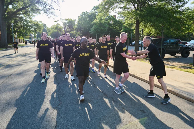 A group in shirts for the US Army outdoors. Some shake hands and smile.
