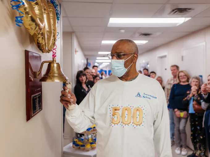 A person wearing a shirt that reads "500" rings a bell in a hospital setting.
