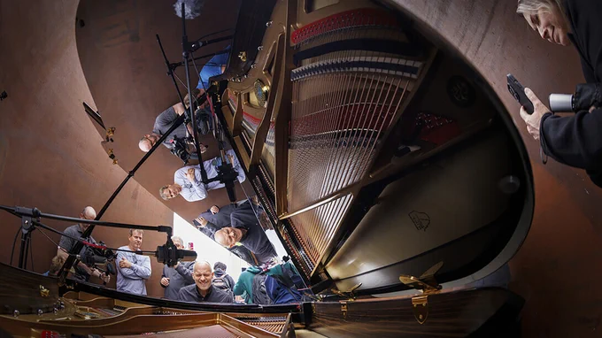 Paul Barnes, Marguerite Scribante Professor of Music (piano) at the University of Nebraska–Lincoln, plays a grand piano in the middle of the "Greenpoint" sculpture on City Campus as a few people watch and film. (Craig Chandler/University Communication and Marketing)