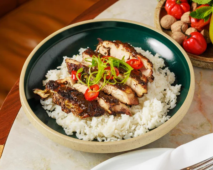 Grilled chicken slices served over a bed of white rice, garnished with sliced red chili peppers and green onions in a green bowl.