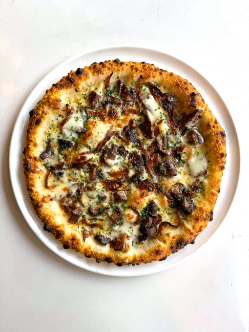 Wood-fired pizza topped with melted mozzarella, mushrooms, and herbs on a white plate.