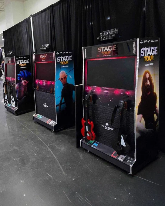 A lineup of Stage Tour demo arcade cabinets is pictured at the IGN Live event, branded with decals featuring the game's models, a widescreen display, and CRKD guitars for gameplay.