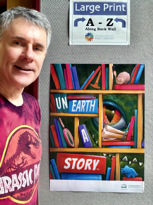 Witmer stands next to a poster at the Athens Public Library declaring June's them of "Unearth a Story", which is the context for his dinosaur exhibit and his presentation of a public dinosaur event at the library next Tuesday, June 16th: https://bit.ly/4xrOiSM.