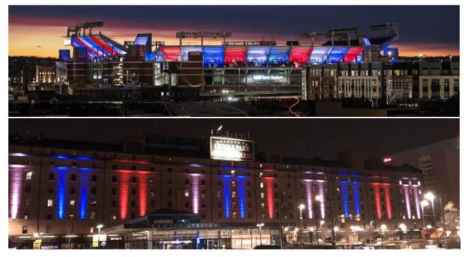 The image features two stadiums illuminated in red, white, and blue lights. The top stadium is M&T Bank Stadium, and the bottom is the Warehouse at Camden Yards. The sky is dark, indicating nighttime.