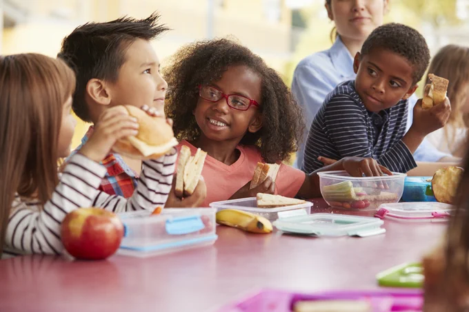 a group of children eat lunch at a picnic table.