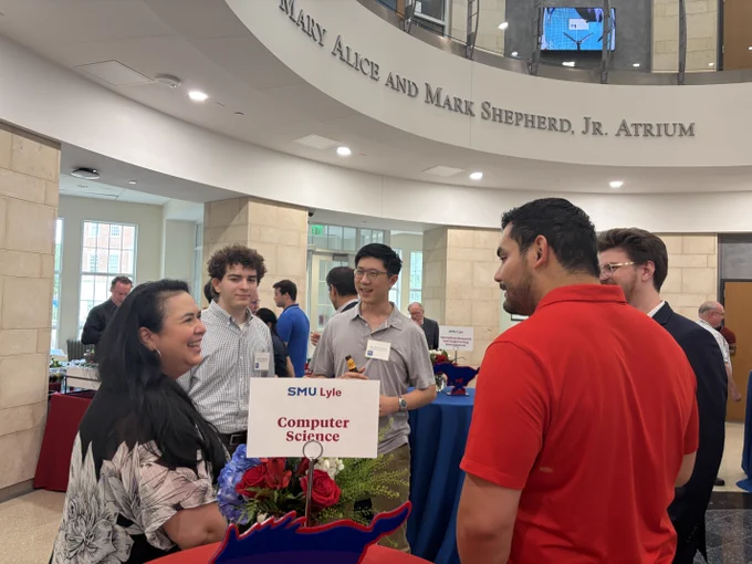 A group of people are engaged in conversation at an event inside the SMU Lyle School of Engineering building. A sign on a table reads "Computer Science." The setting is an atrium with visible signage for "Mary Alice and Mark Shepherd, Jr. Atrium.