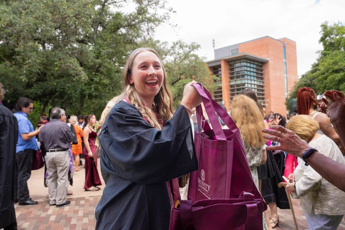 A graduate with blonde hair takes a maroon Trinity University swag bag.