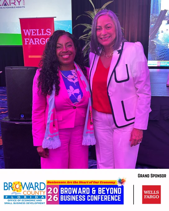 Two smiling people standing in front of a stage at the Broward & Beyond Business Conference.