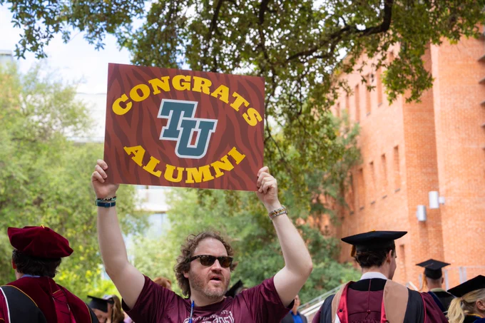 An alumnus holds up a sign outside that says Congrats TU Alumni.