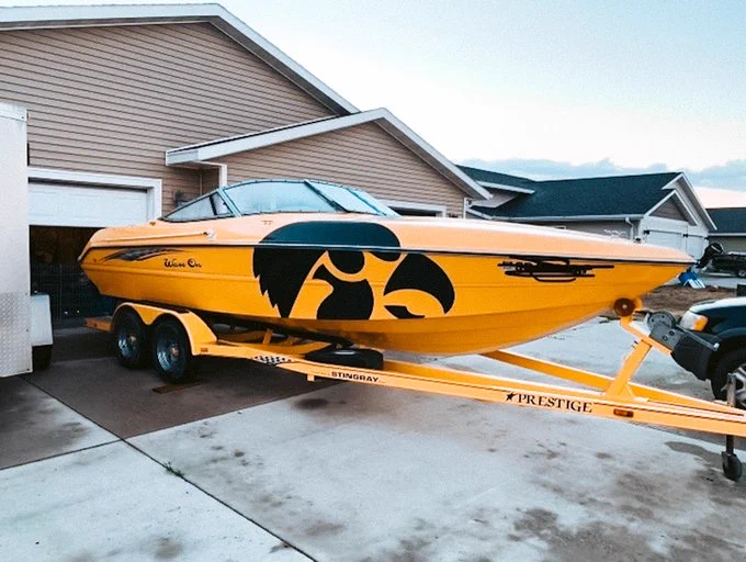 Speedboat with a large Tigerhawk logo on the side, parked on a trailer in a residential driveway next to a beige garage and house.