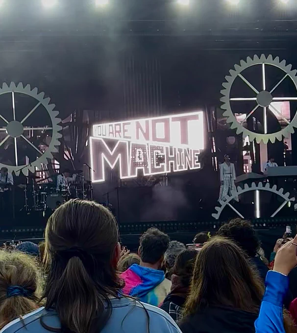 A picture of a stage with gears on it. The LED screen says “You are not machine”