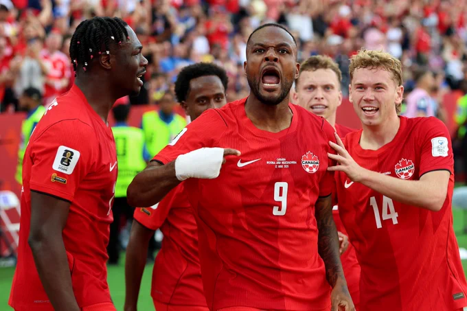 Cyle Larin celebrates scoring for Canada against Bosnia in the World Cup, pointing to his chest with teammates surrounding him