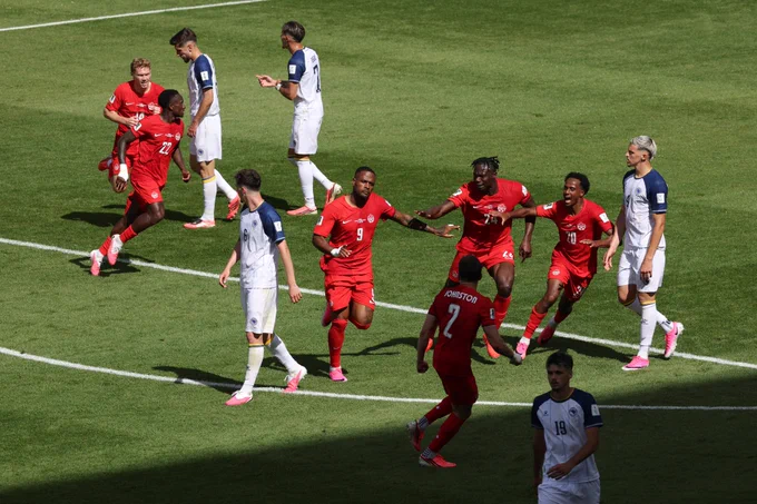 Cyle Larin celebrates scoring for Canada against Bosnia in the World Cup with teammates and dejected opponents surrounding him