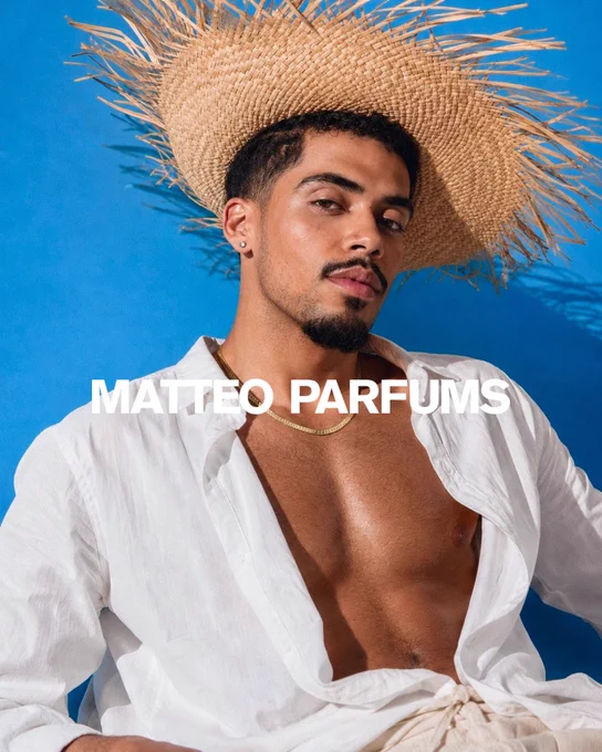 Matthew J. Sánchez, Founder & Perfumer of MATTEO PARFUMS, seen in new editorial campaign shoot for his fine fragrance brand—promoting Lovers’ Dew. He’s wearing a decorative straw hat, white linen button up shirt, beige linen trousers, and wearing his gold jewelry. “MATTEO PARFUMS” branding is overlayed.
